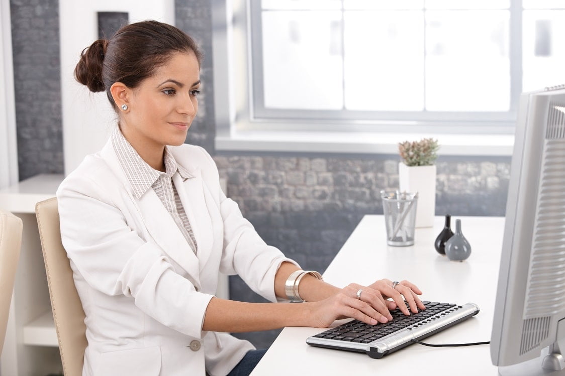 A professional woman in a white blazer typing on a keyboard at her desk, symbolizing the process of creating or managing CMC documentation in a structured office environment.