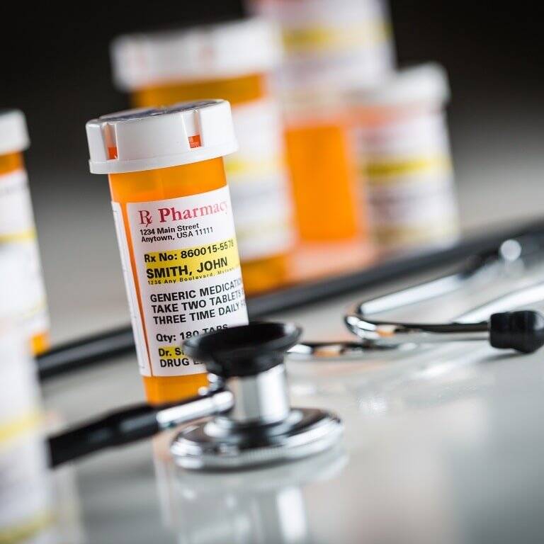 Prescription medication bottles with one labeled for ‘Smith, John’ in focus, accompanied by a stethoscope, illustrating healthcare and global labelling standards for consistent and clear medication instructions.