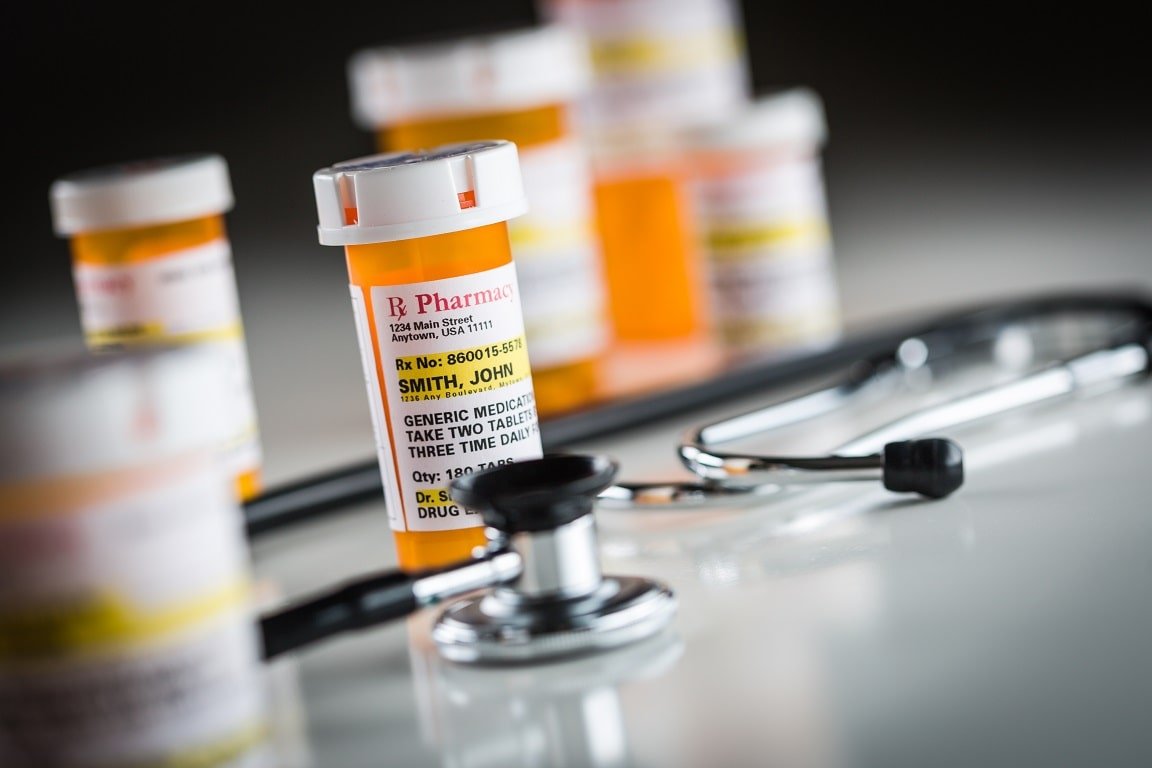 Prescription medication bottles with one labeled for ‘Smith, John’ in focus, accompanied by a stethoscope, illustrating healthcare and global labelling standards for consistent and clear medication instructions.