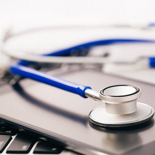 A close-up of a stethoscope resting on a tablet and laptop keyboard, symbolizing digital tools in medical documentation.