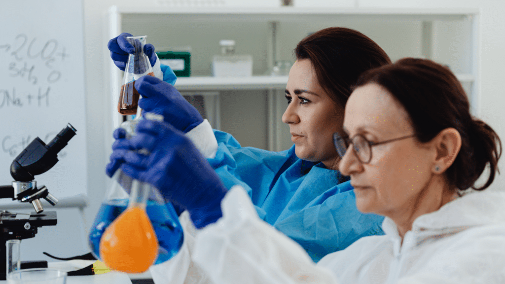 Pharma lab technicians review chemicals in beakers, verifying evidence that supports authoritative, traceable Quality and CMC content as regulated information changes across the product lifecycle.